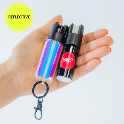 Hand holding a shiny blue pepper spray canister with a keychain with a practice spray canister with a reflective label on a white background